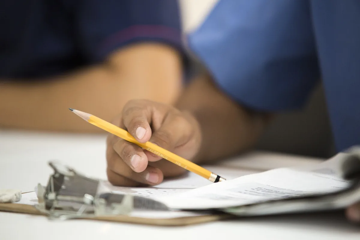 Well-lit workspace with hands filling a form beside a camera and notebook; printed checklist visible but not legible