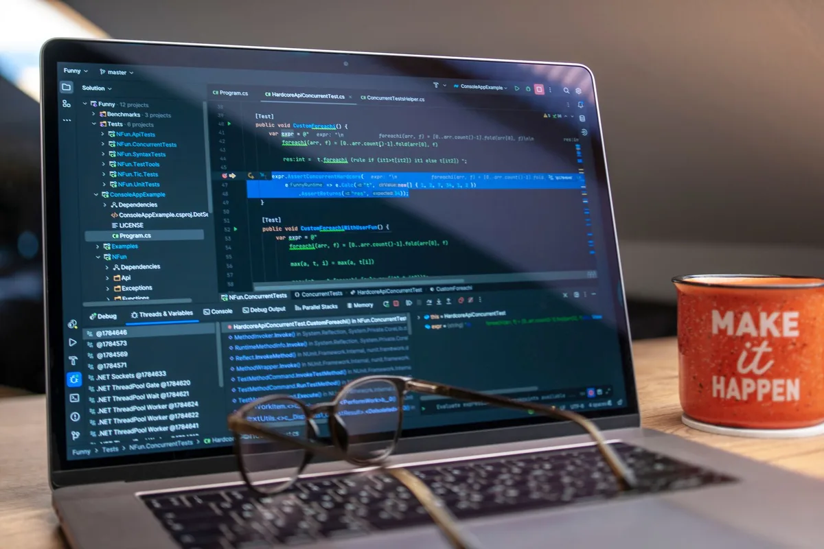 hands typing on a laptop showing code editor, a closed notebook and a calculator at the side