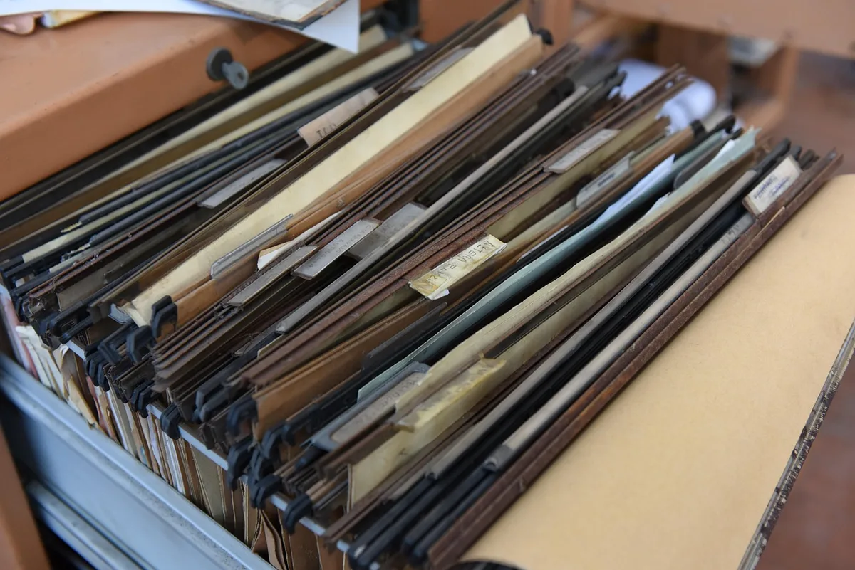 A clean training folder marked "attestation" on a bright table, beside a pen and a smartphone showing an email inbox, documents stacked and a blurred calculator in background