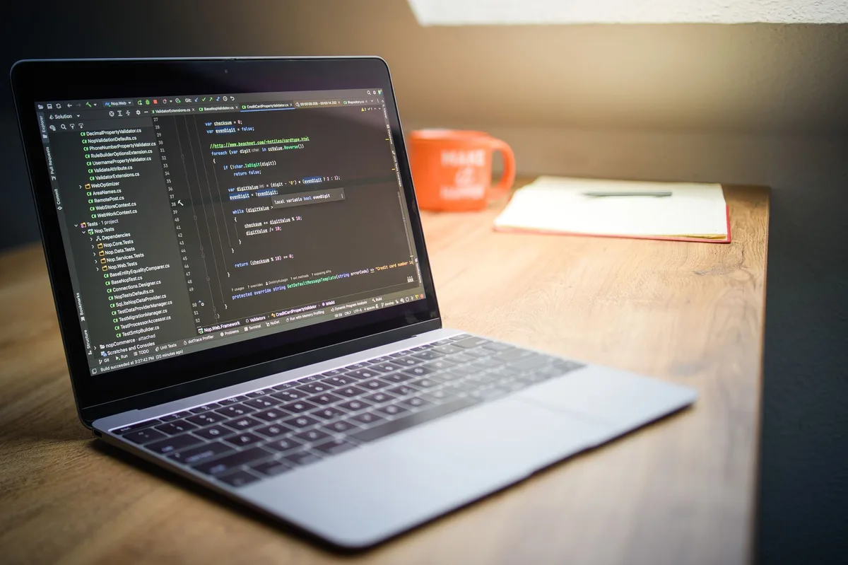 A neat home desk with a laptop showing code editor, a notepad with handwritten notes, and a cup of coffee nearby