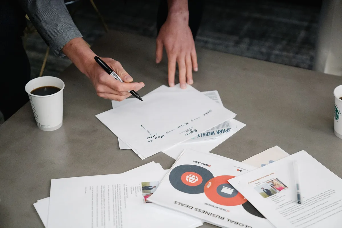 hands filling a training application form on a desk with paperwork and a pen, a blurred calculator in background
