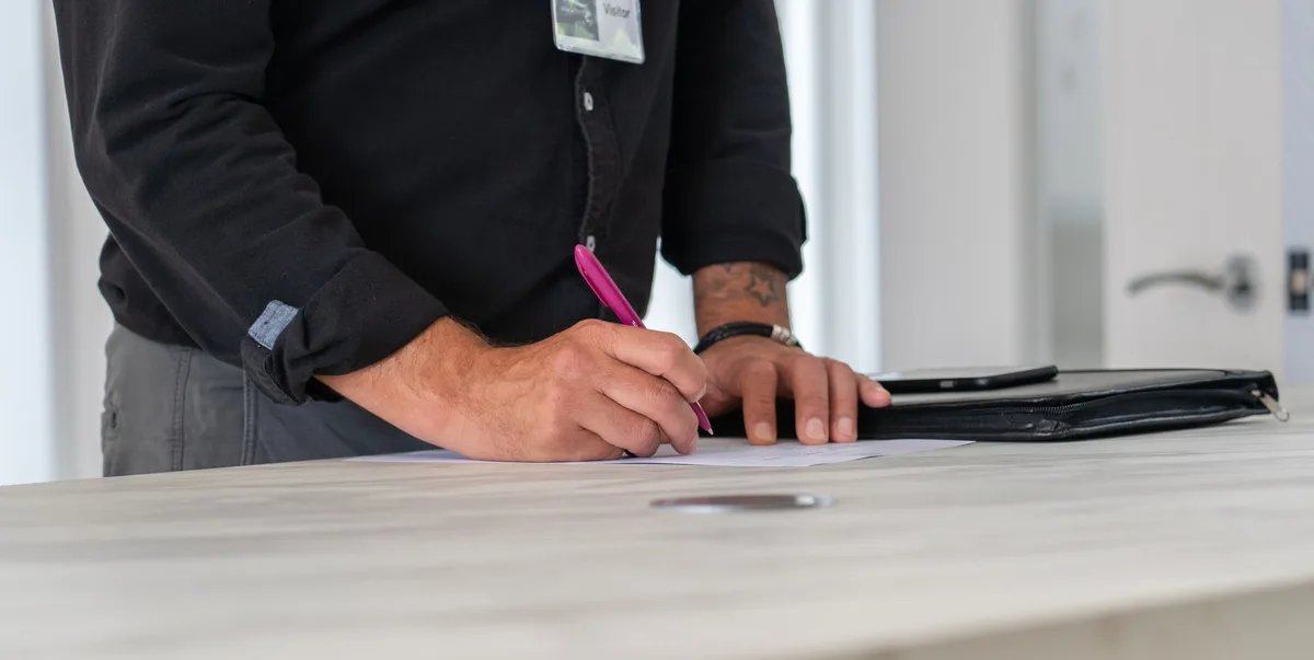 A well-lit desk with hands filling an official training form, a closed booklet labelled "documents" blurred in the background