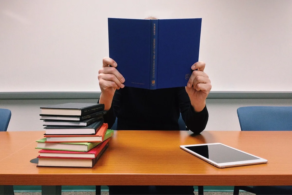 A tidy desk with printed exam forms, a pen, and a closed laptop next to a small stack of culinary textbooks; no logos or personal items