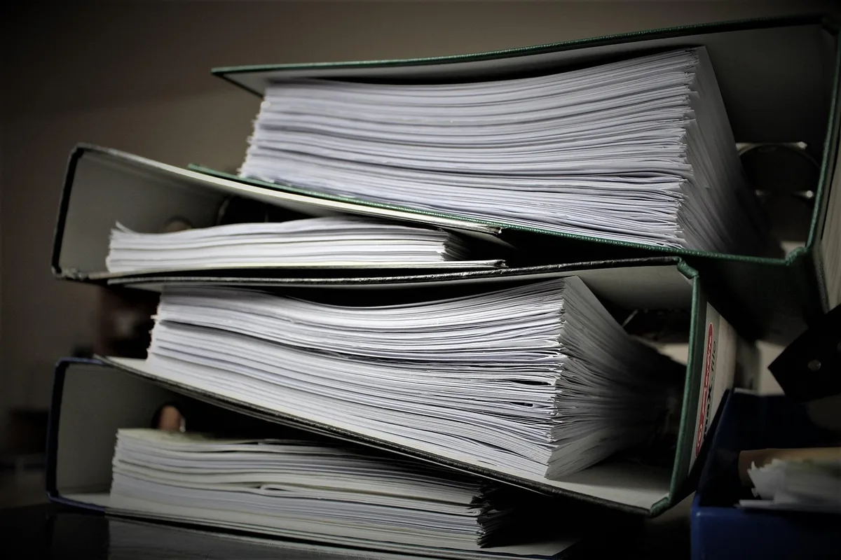 A bright office desk with hands filling out certification paperwork, documents and a laptop visible but no logos