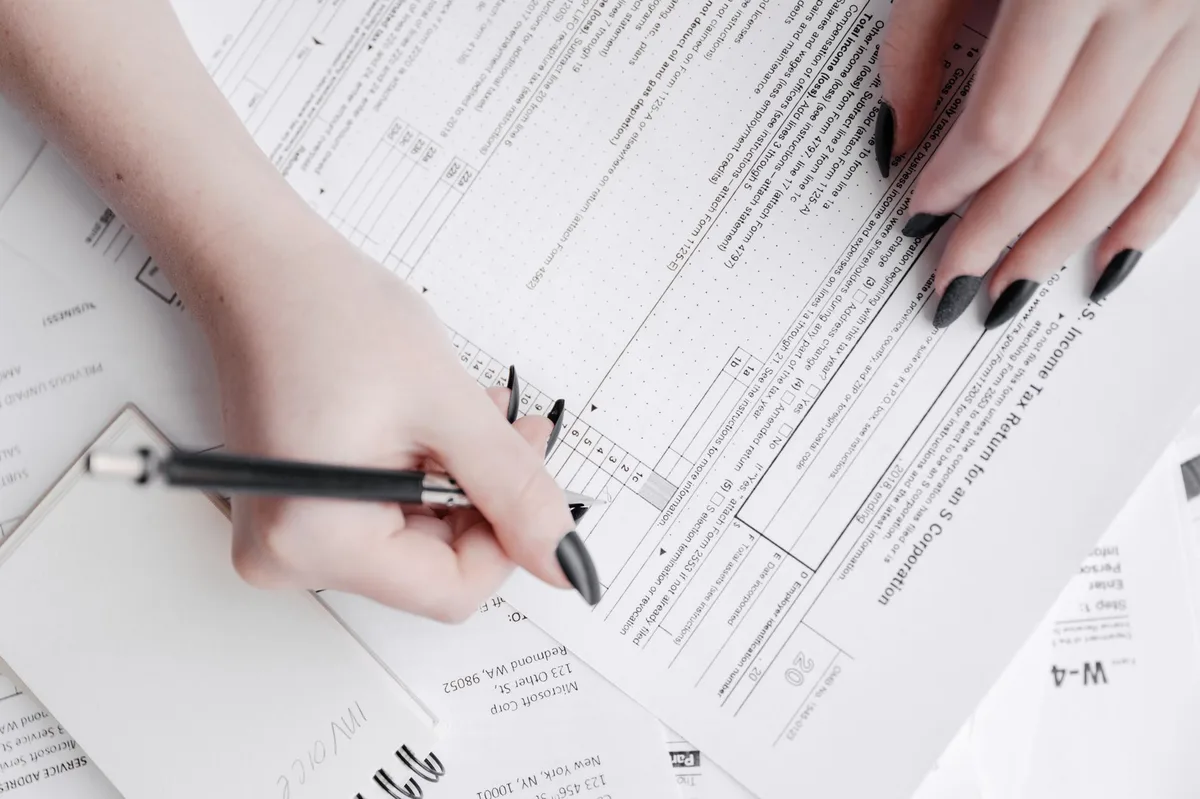 Two anonymous hands filling a printed application form on a desk with a pen and a smartphone showing a training platform