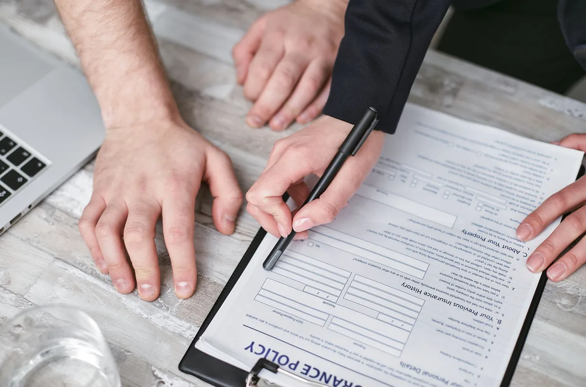two anonymous hands filling a training enrollment form on a desk with a closed laptop nearby